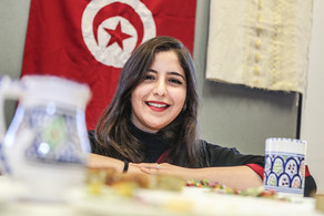 Internationale Studierende vor tunesischer Flagge Eine internationale Studierende lächelt in die Kamera. Im Hintergrund hängt eine Tunesienflagge.